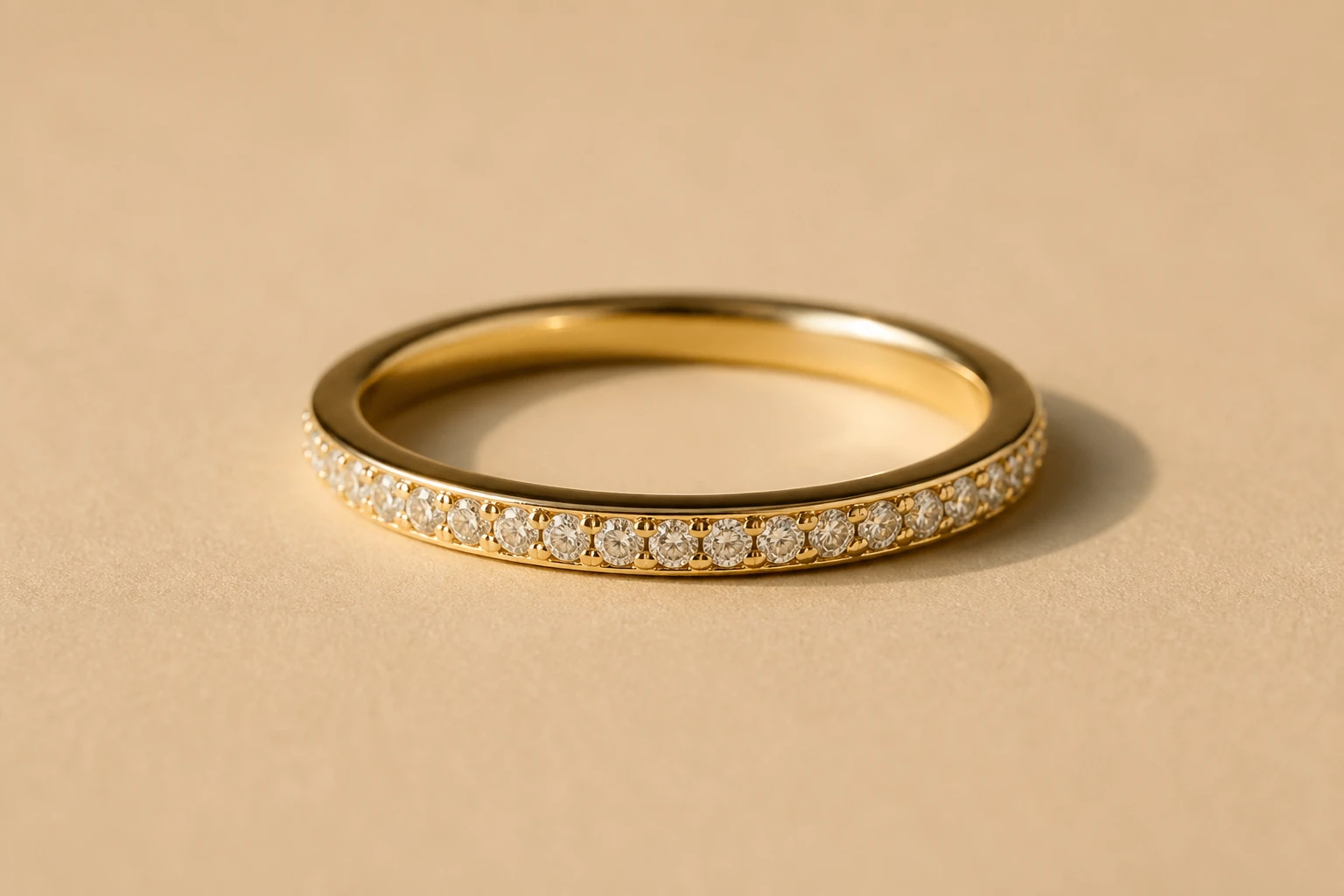 Aliança fina de ouro amarelo com cravação de diamantes minúsculos em meia volta, macro sobre fundo areia